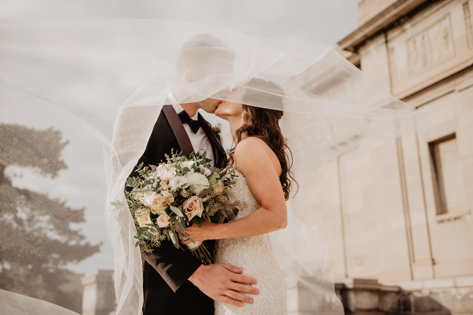 A couple kissing beneath a veil lifted by the wind