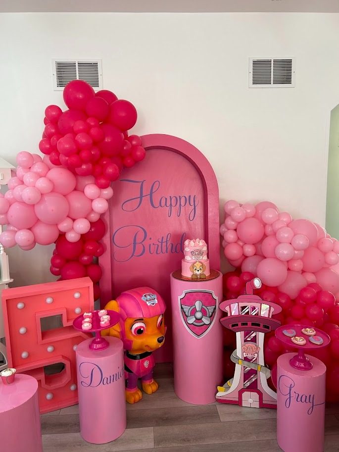 A pink balloon arch birthday setup with marquee letters