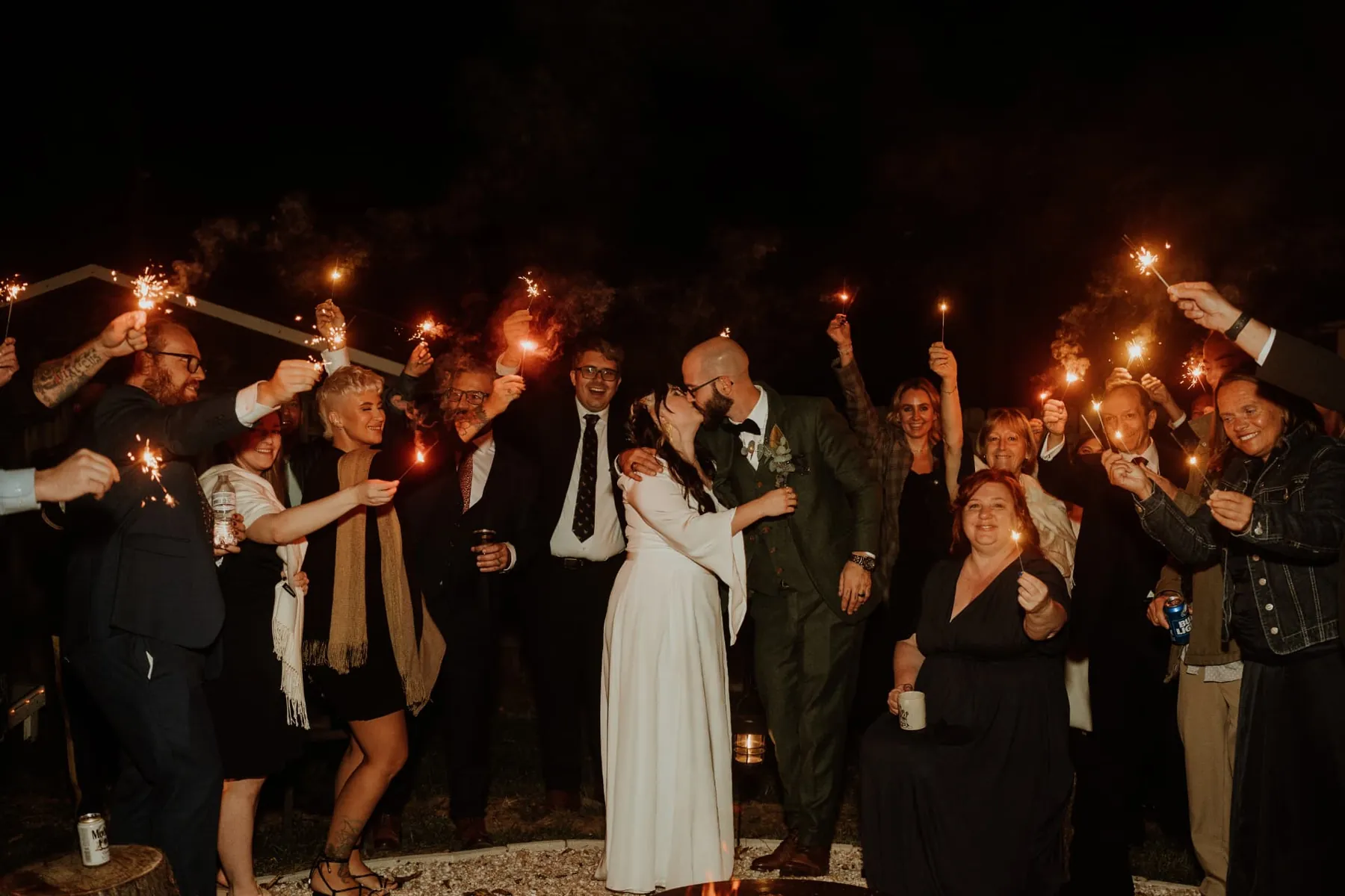 Guests raising sparklers as the couple kiss at the send off