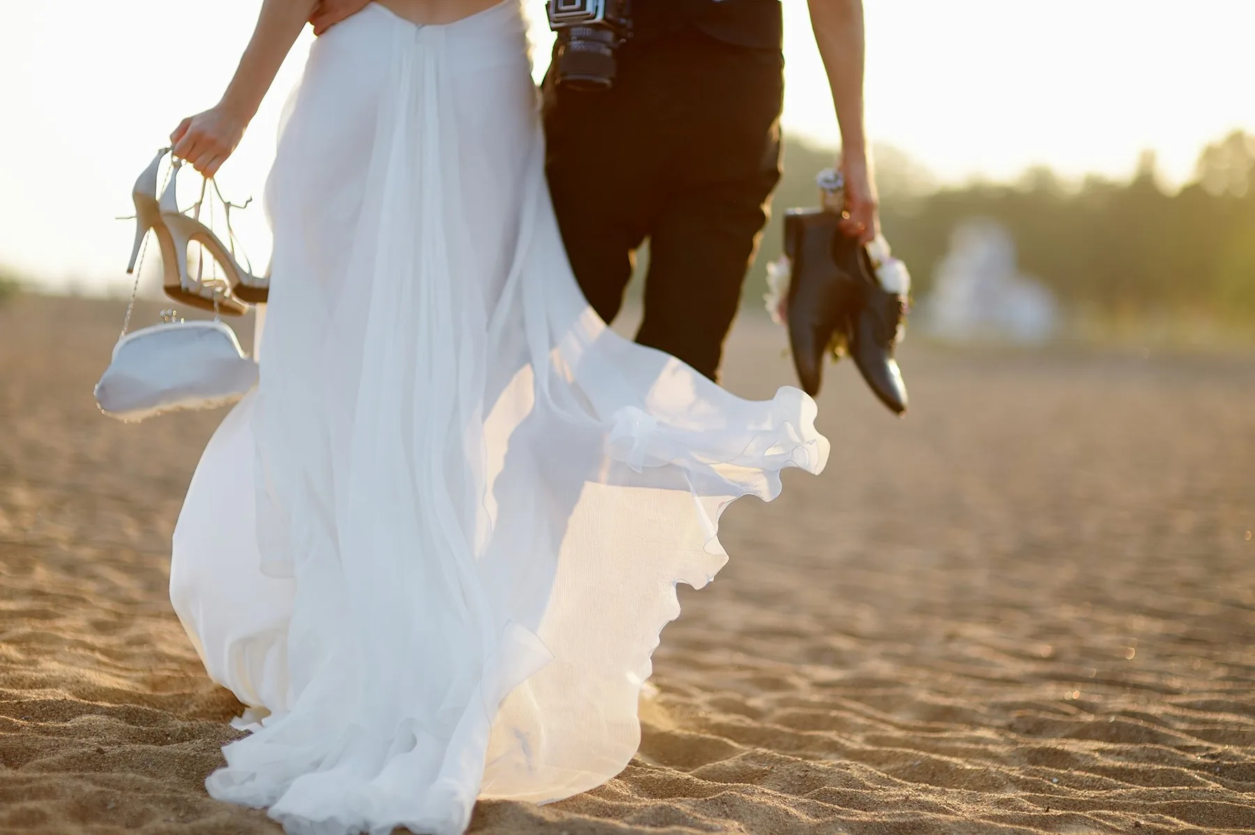 A couple holding hands walking on the beach with their shoes off