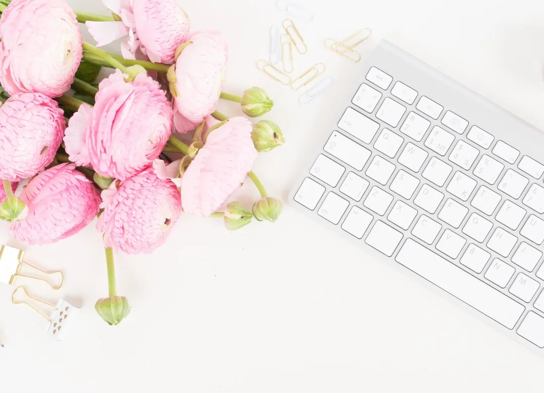 A keyboard on a desk adorned with pink flowers