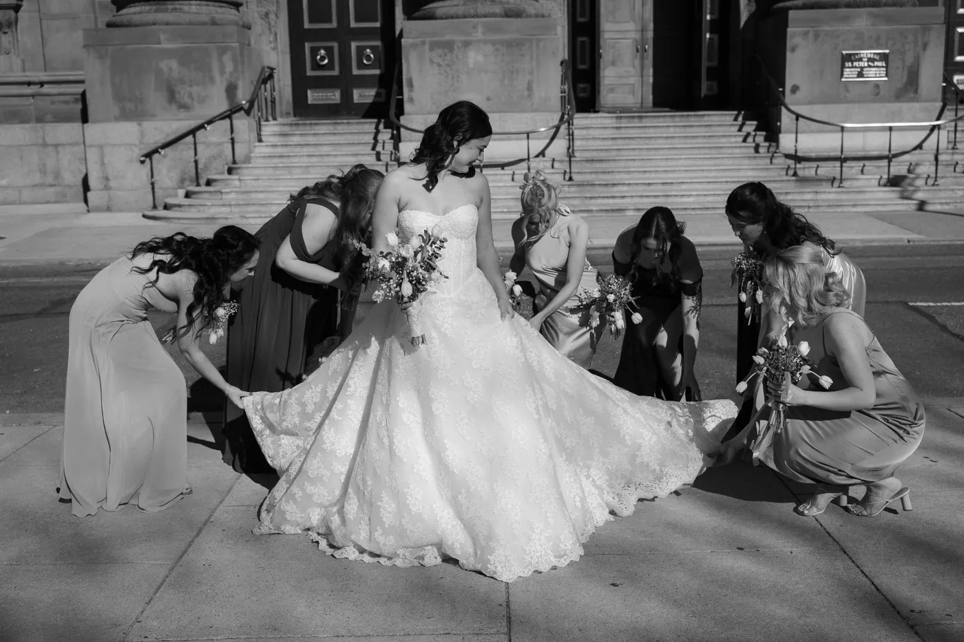 Bridesmaids gathered around the bride on stone steps, in black and white
