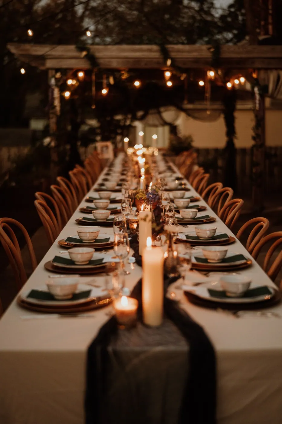 A candlelit banquet table set beneath string lights